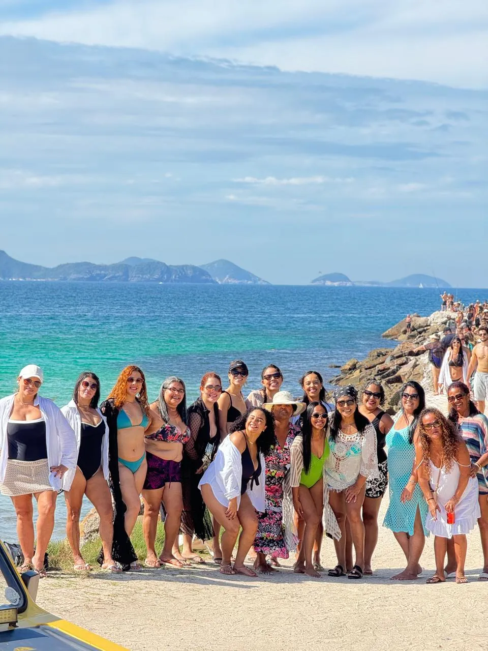 Grupo de viajantes reunido na faixa de pedras com o mar ao fundo
