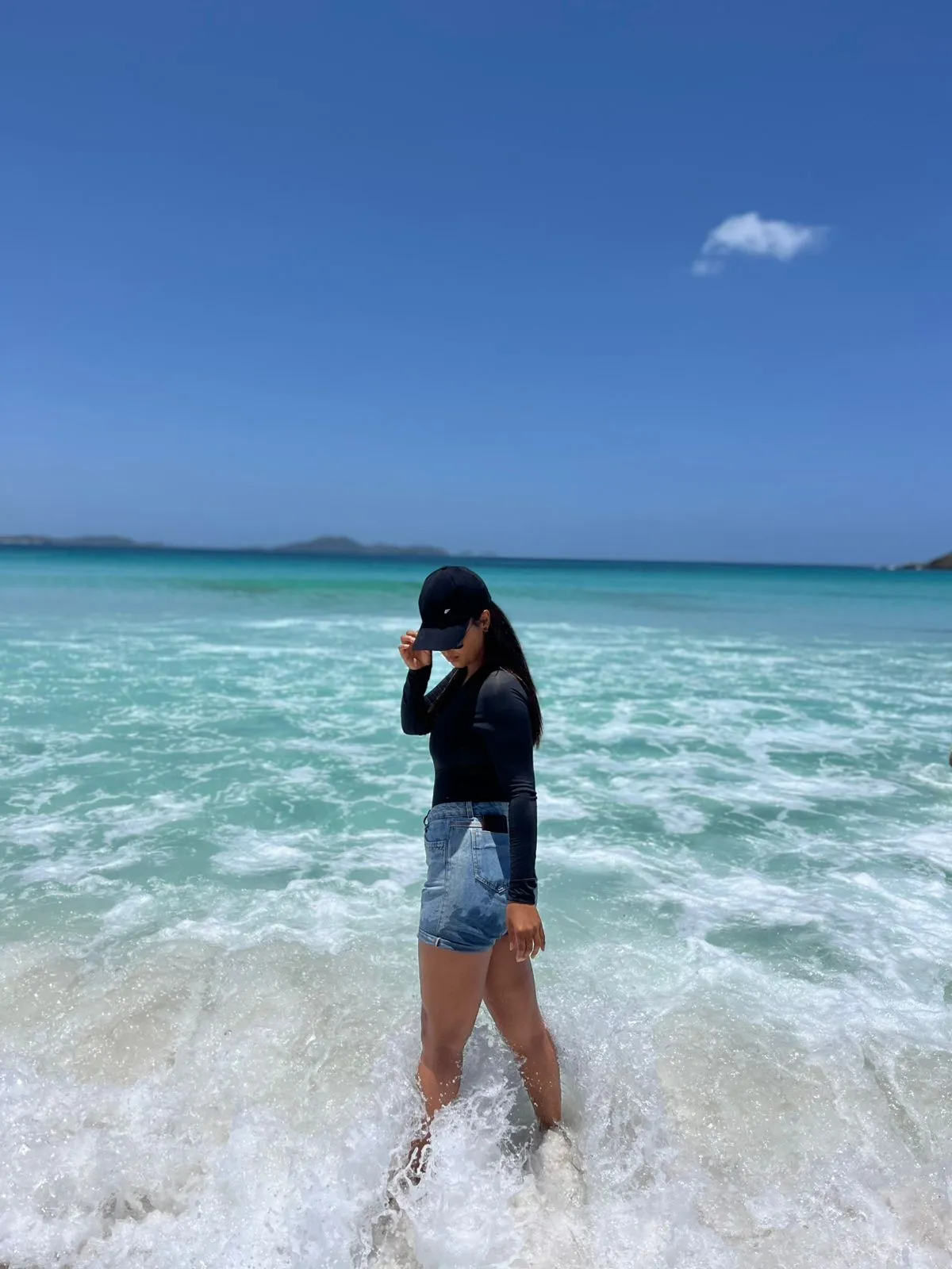 Mulher em pé na arrebentação, com o mar azul de Arraial do Cabo ao fundo
