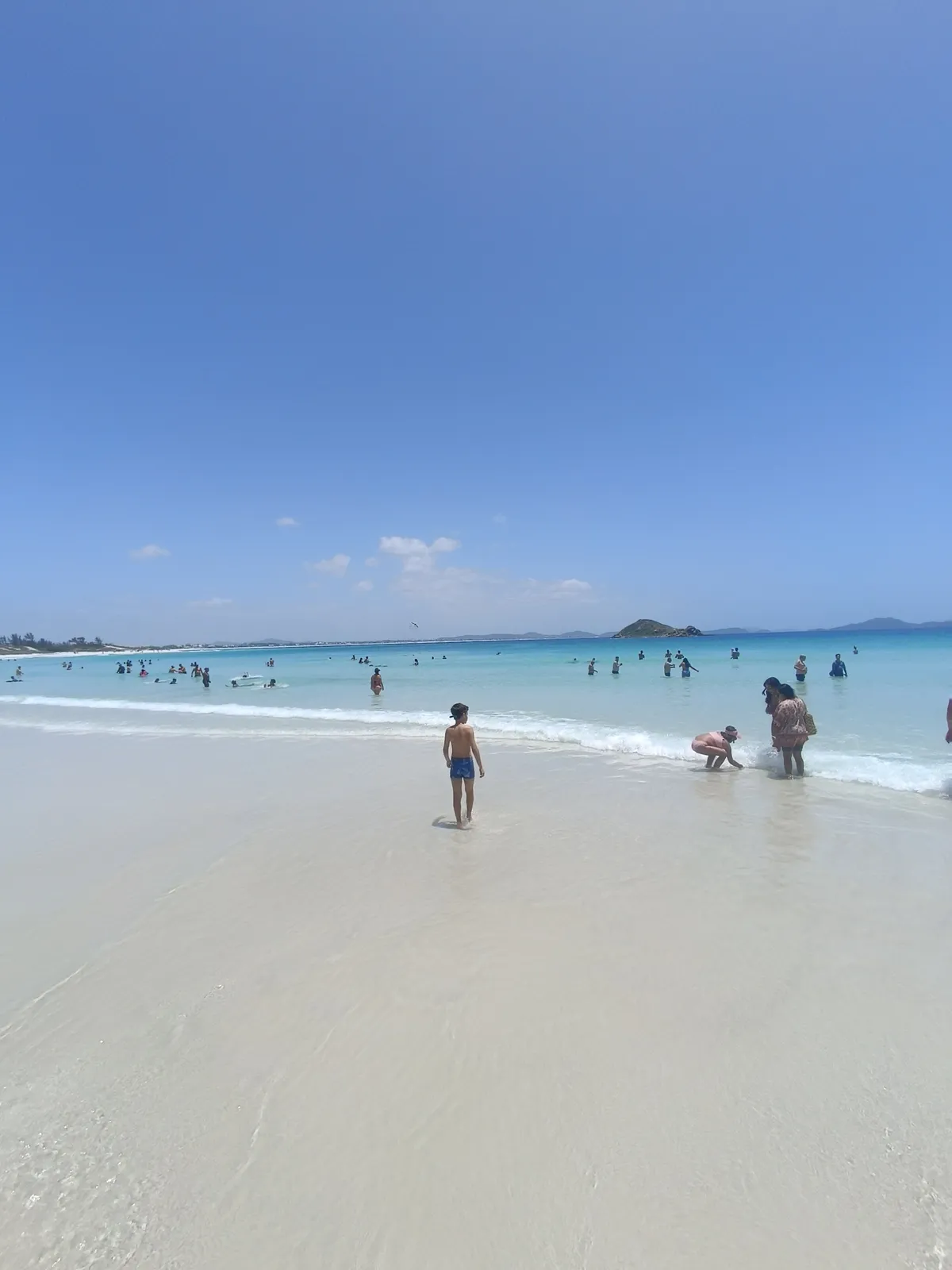 Faixa de areia branca e mar raso de Arraial do Cabo com banhistas
